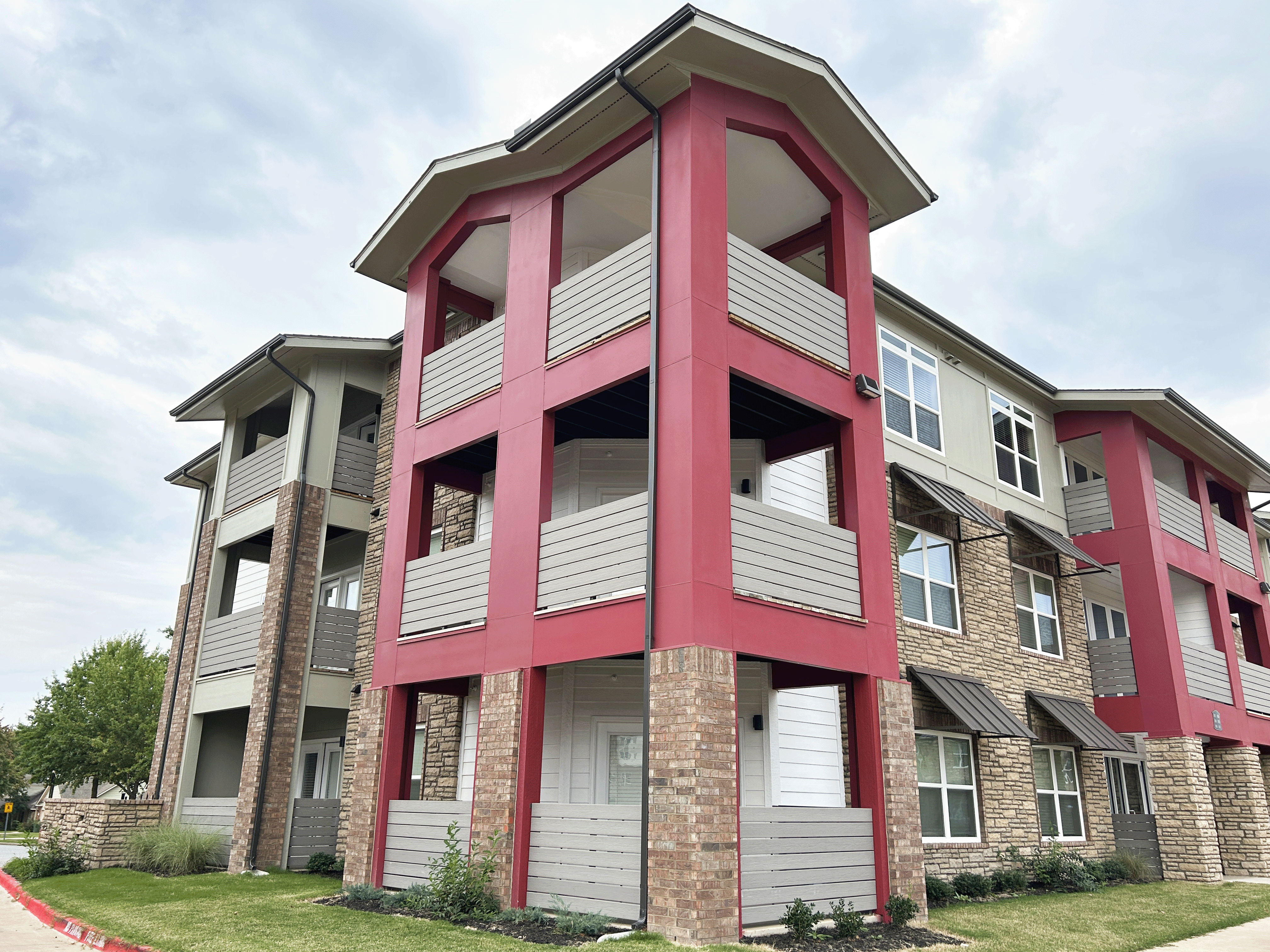 A red and beige apartment building with a cloudy sky in the background.
